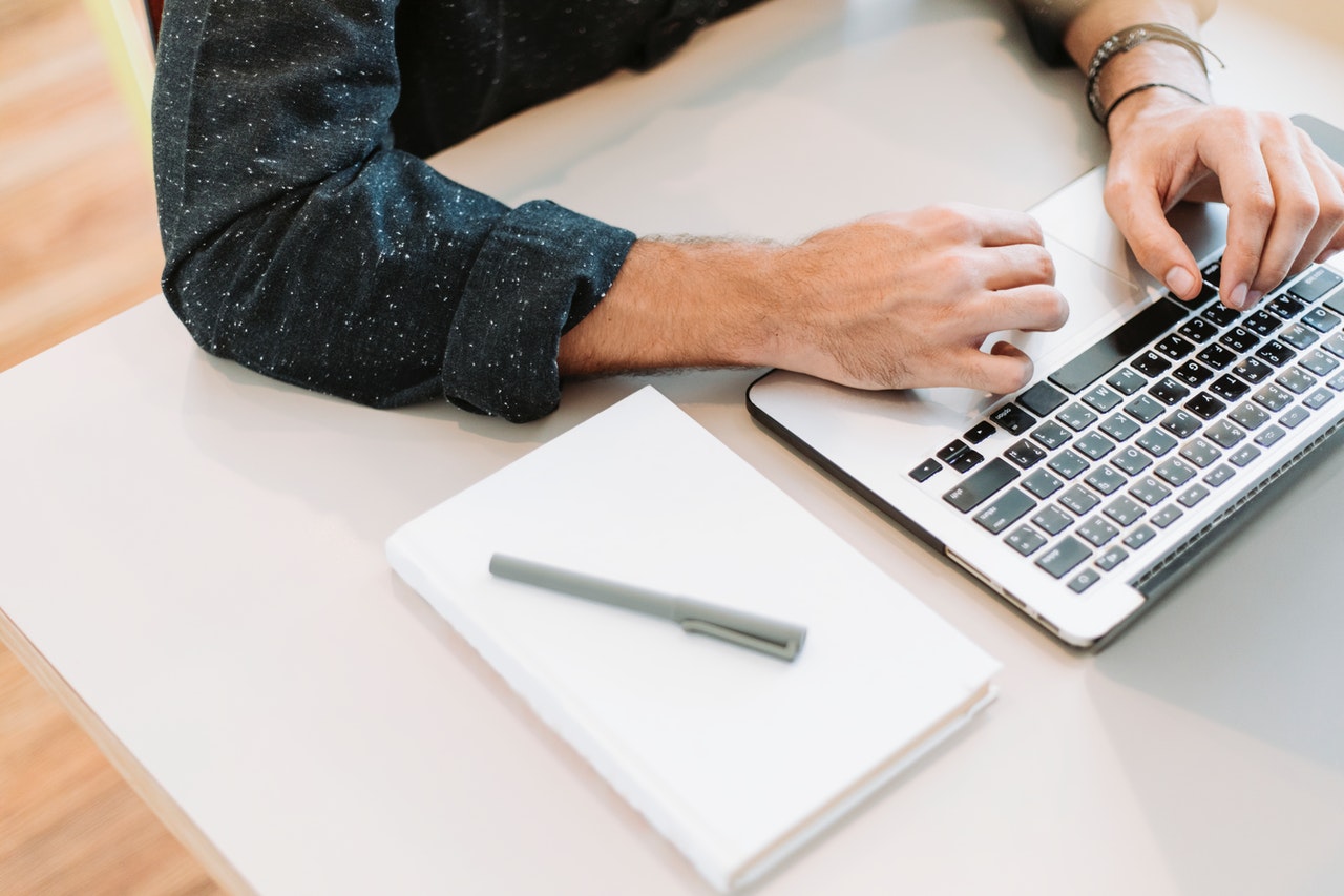 man typing resume objective with a blank paper and pen beside the laptop