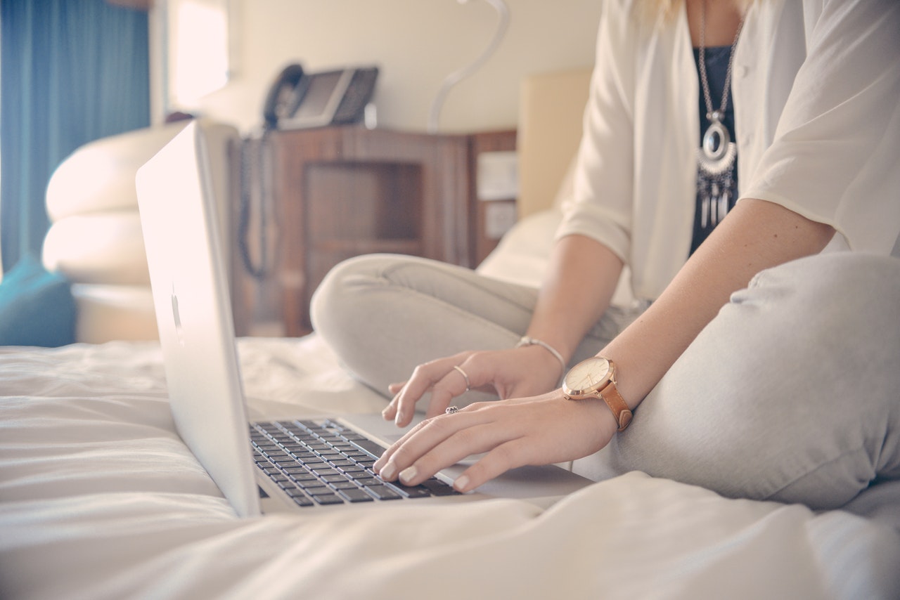 woman on top of the bed browsing resume for free online using a laptop