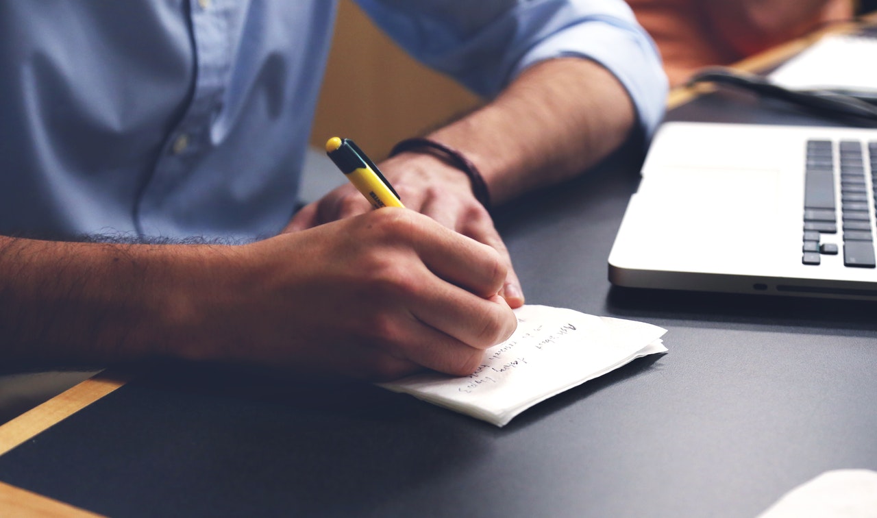 a man writing down resume prime tips on a piece of paper near a laptop